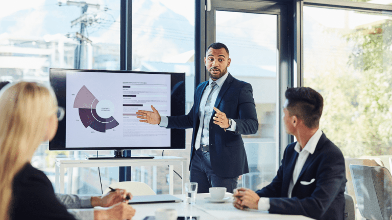 A professional presenting a business pie chart to employees during a payroll and HR outsourcing meeting.