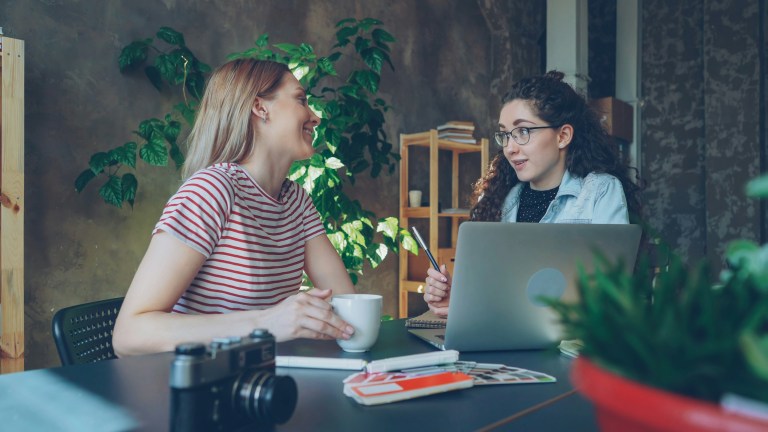 Two women talking next to a laptop about HR outsourcing and staying compliant.
